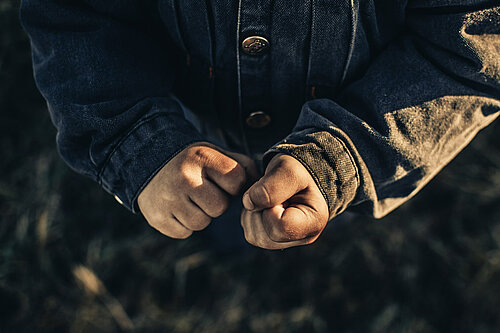 Photo shows a person's clenched fists, they are wearing a grey jacket.